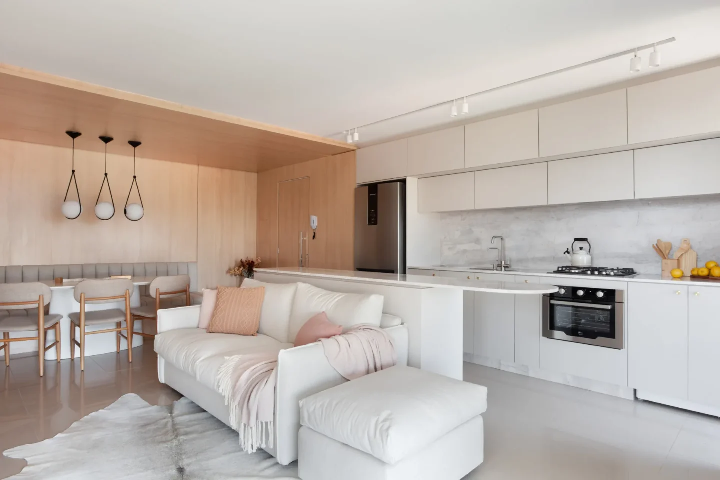 Vista do living para a cozinha aberta, com bancada de mármore claro e marcenaria off-white