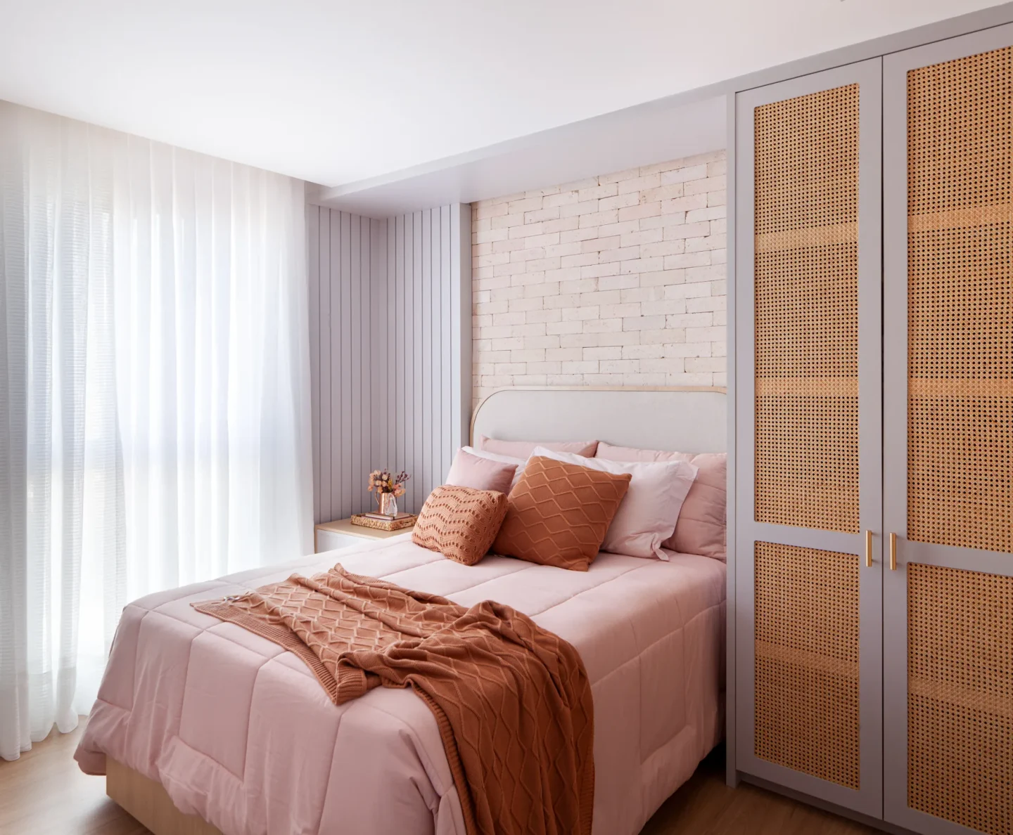 Dormitório com parede de tijolo claro, cabeceira estofada e roupa de cama em rosé e terracota