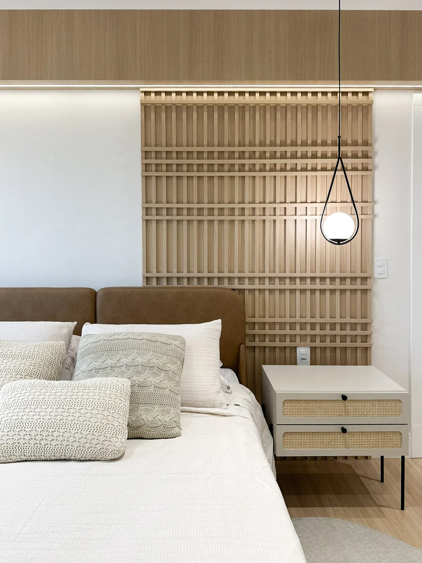 Quarto com painel ripado de madeira, pendente de vidro e criado-mudo com palhinha