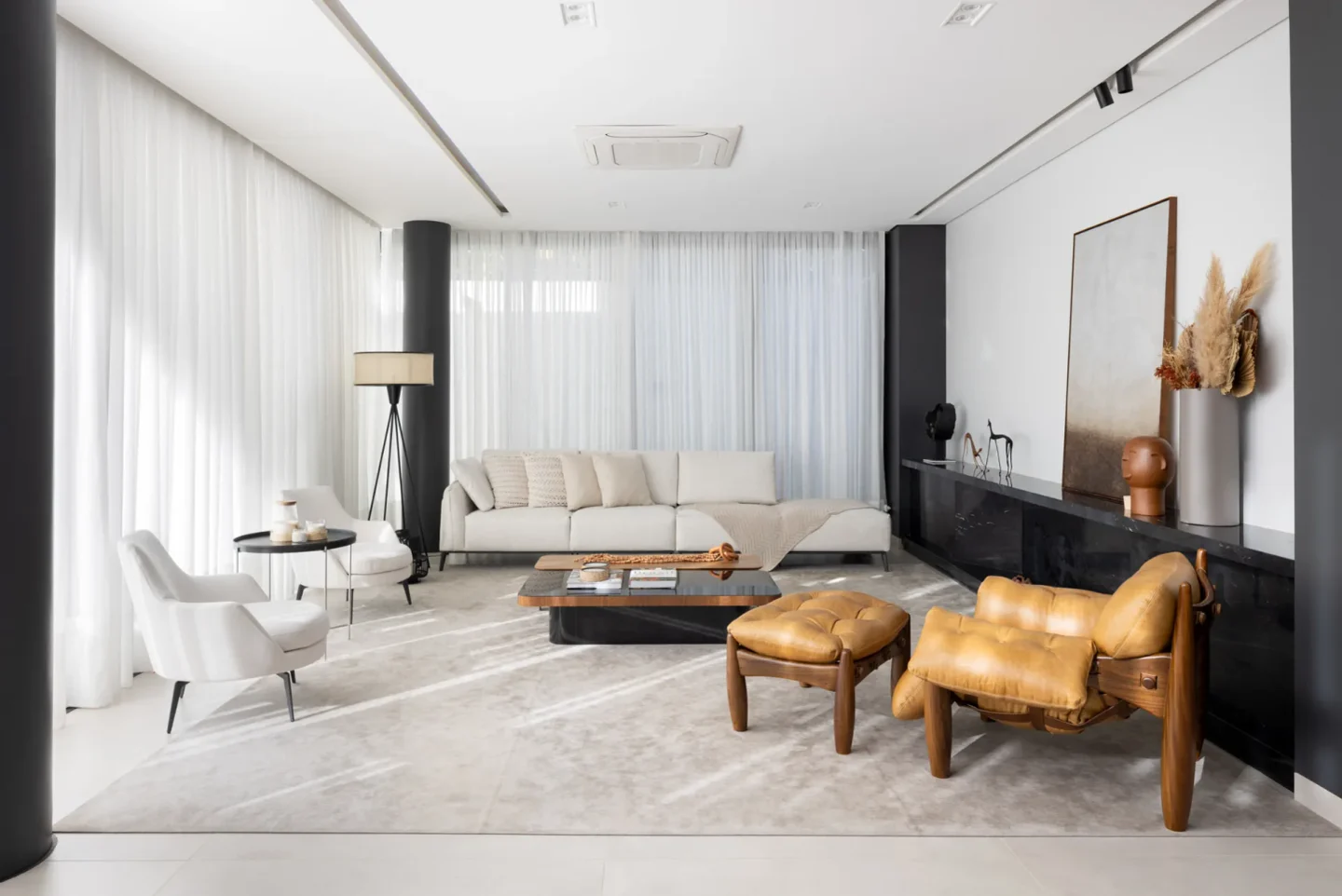 Living claro com sofá off white, Poltrona Mole de couro caramelo e aparador de mármore escuro